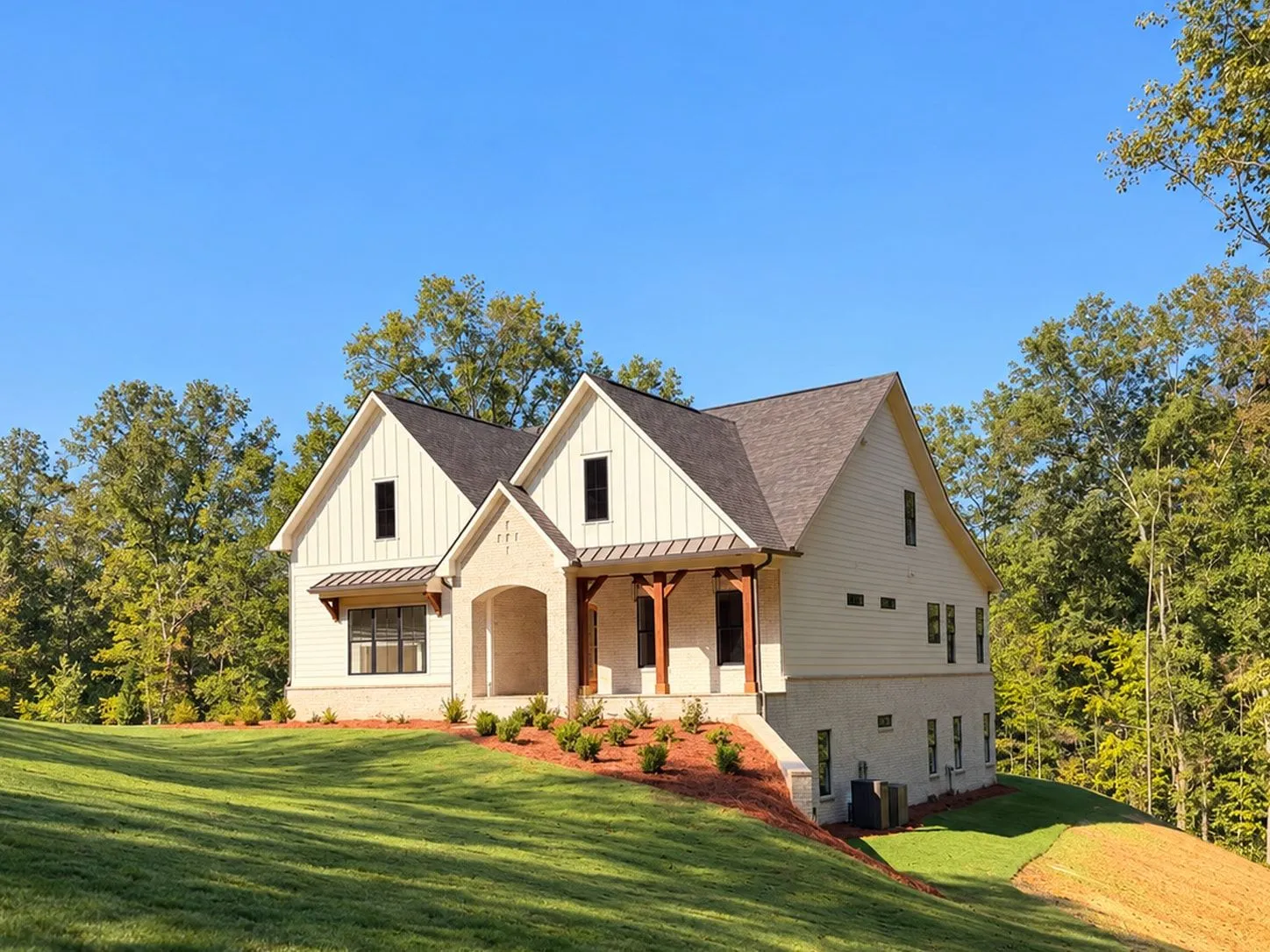 Cream brick and board-and-batten house with an arched brick entry and a covered porch on wood posts, above a sloping lawn
