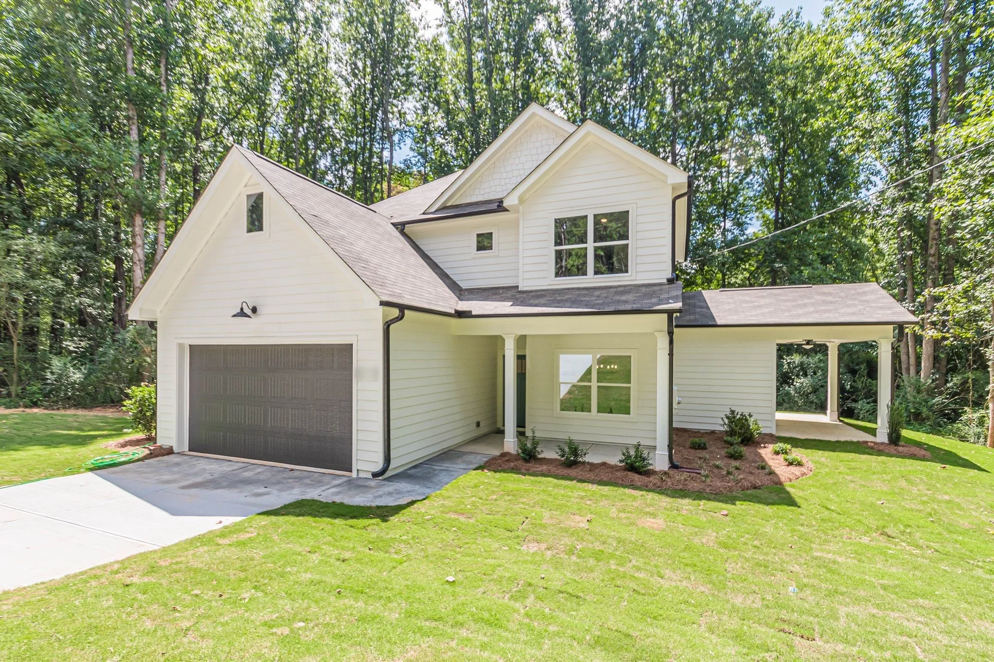 White two-story house with a wide garage door, a covered front porch, and a new lawn, with tall woods behind